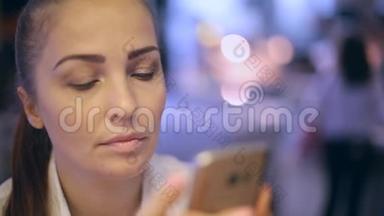 一个年轻的女人坐在快餐店里，拍自拍，在智能手机屏幕上看她的照片。